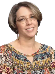 Professional woman smiling, wearing glasses and a colorful patterned blouse.